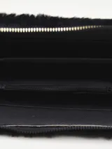 Billetera negra de piel sintética con textura de pelo, cierre de cremallera dorada y pompón colgante. Tiene bordado en azul la palabra "PINK".