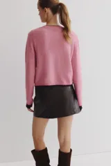 Saco corto de punto fino, color rosado, con escote redondo, cierre frontal con botones y detalles de ribetes en contraste en cuello, puños y ruedo.