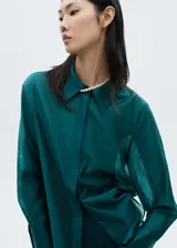 Camisa de vestir verde esmeralda de corte recto, con cuello camisero, cierre frontal con botones ocultos y mangas largas con puños abotonados.
