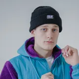 Gorro tipo beanie de tejido acanalado color morado, con borde doblado y parche rectangular negro con el logo "PULAU" y el texto "WEAR MORE & WORRY LESS ESTABLISHED IN 2023 IN MONTEVIDEO, UY".