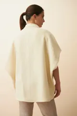 Chaleco color crema de lana sin teñir, corte recto, con cuello y solapa pronunciadas, broches a presión y bolsillos ojal.