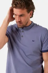 Remera de manga corta color azul grisáceo con cuello mao y tapeta de botones. Los puños de las mangas y el cuello son de color azul marino contrastante. Presenta un pequeño logo bordado en el pecho.
