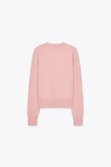 Chaqueta rosa de punto con cuello redondo y manga larga. Tiene hilo metalizado y cierre frontal con botones en relieve con forma de flor.