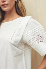 Vestido corto color crema, de corte recto y cuello redondo. Presenta mangas cortas amplias con calados geométricos en el ruedo.