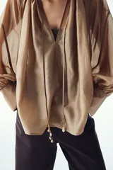 Blusa color dorado de lyocell con cuello redondo con cordón ajustable, abertura en V y mangas globo largas con puños vueltos con abertura y botón.