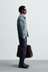 Cazadora de denim de algodón de corte regular, color azul medio lavado. Presenta cuello solapa, manga larga con puños abotonados, dos bolsillos de solapa en el pecho y bolsillos laterales en la costura de la cadera. Cierre frontal con botonadura.