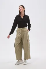 Pantalón cargo de algodón color verde oliva, tiro bajo, con cintura ajustable mediante cordón y piernas anchas y rectas. Presenta bolsillos cargo en los laterales.