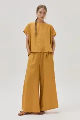 Pantalón de lino color mostaza, de corte palazzo, con lazo en la cintura, pinzas en el frente y bolsillos laterales.