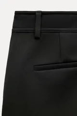 Pantalón negro de tiro medio, con trabillas en la cintura, bolsillos laterales y de vivo en la espalda, raya planchada en el delantero y pierna recta.