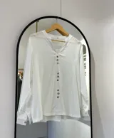 Blusa blanca de manga larga regulable, con escote en pico y botones frontales.