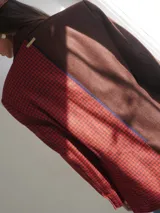 Blazer oversize con diseño asimétrico que combina dos tweeds contrastantes: uno marrón liso y otro blanco y negro con estampado pata de gallo. Tiene botones de strass y un pin de salchicha.