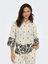 Camisa color crema con estampado de hojas y flores negras, cuello camisero, mangas 3/4 amplias y cierre frontal con botones.