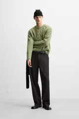 Sweater verde claro de punto con cuello redondo y mangas largas. Presenta diseño de trenzas en el centro y en las mangas.