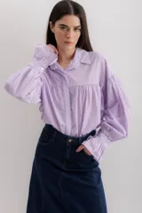 Camisa de algodón a rayas verticales color lila y blanco, con cuello camisero, mangas largas abullonadas con puños elásticos y corte holgado.