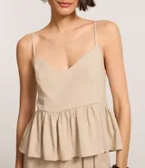 Blusa sin mangas color beige, con escote en V, breteles finos ajustables y peplum con volados en el bajo. Presenta lastex fruncido en la espalda.
