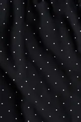 Mono corto negro con estampado de lunares blancos. Presenta escote cuadrado, breteles anchos con volados y elástico revestido en la cintura.