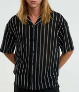 Camisa masculina modelo boxy, confeccionada en punto, con cuello polo, manga corta, cierre por botones y estampa de rayas verticales blancas sobre fondo negro.