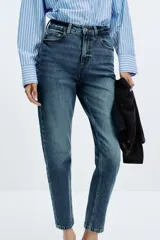 Pantalón de jean azul de tiro alto, corte mom fit, tobillero y con cinco bolsillos. Cierre frontal con cremallera y botón.