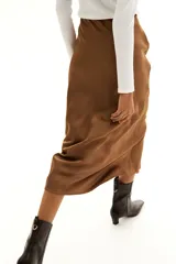 Pollera midi color marrón con leve brillo y caída suave. Modelo de tiro alto con elástico oculto en la cintura y leve vuelo en el bajo.