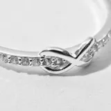 Anillo plateado con forma de infinito y pequeños brillantes incrustados.