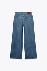 Pantalón de jean azul de corte wide leg, tiro alto, con cinco bolsillos y cierre frontal con cremallera y botón.