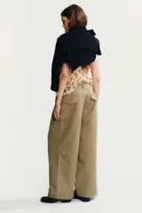 Pantalón color beige de tiro medio con trabillas, bolsillos laterales, de plastrón en pierna y detalle de solapas en espalda. Detalle de pinzas en delantero y cierre frontal con cremallera y ganchos metálicos.