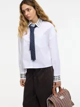 Camisa cropped blanca de algodón con tachas plateadas en cuello y puños, botones frontales, bolsillo en el pecho y pinzas en la espalda.