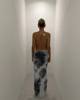 Vestido largo ajustado, sin mangas, con escote drapeado tipo halter y textura plisada. Presenta un estampado tie-dye en tonos blanco y negro/azul oscuro.