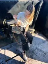 Cartera bandolera pequeña de cuero con estampado animal print, forro de tela y correa larga de cuero marrón.