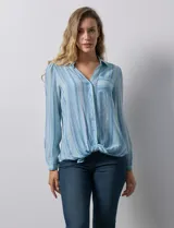 Camisa de gasa celeste con estampado de rayas verticales en tonos azules, rosas y verdes. Tiene cuello con solapa, escote en V, abertura central con botones, bolsillo aplicado en el pecho y terminación anudada en la parte delantera.