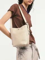 Cartera tipo tote confeccionada en cuero vacuno color crudo, con textura tipo piel de cocodrilo. Tiene correa larga al hombro y apliques metálicos con el logo de la marca. Incluye sobre interno desmontable con cierre.