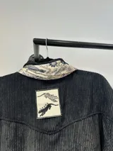 Sobrecamisa negra de pana con cuello camisero y cierre frontal con botones.