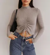 Sweater corto de lanilla color gris con cuello alto y mangas largas. Presenta un frunce central con cordones ajustables.