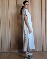 Vestido largo color crudo con cuello redondo y mangas cortas con ribete negro. Tiene corte recto y aberturas laterales en el ruedo.