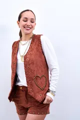 Chaleco marrón de gamuza sintética con apliques de flores y tachas doradas.