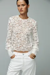 Top de encaje blanco con cuello redondo, mangas largas abullonadas y puños con botones metálicos.