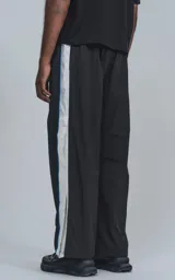 Pantalón deportivo negro de nylon con cintura elástica, cordón ajustable y aberturas laterales con broches a presión.