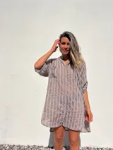 Camisero corto color habano con bordado de líneas verticales blancas. Tiene cuello camisero, mangas cortas y cierre frontal con botones.