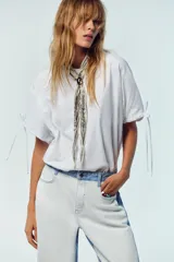 Camiseta blanca de algodón con cuello redondo, corte recto y mangas cortas ajustables con lazadas.