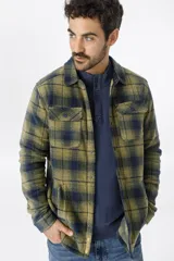 Camisa polar escocesa a cuadros en tonos verde oliva y azul marino, con cuello clásico, cierre frontal con botones, dos bolsillos de parche con solapa abotonada en el pecho y corte recto.