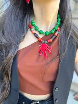Collar corto con cuentas de coral, cerámica y acrílico en tonos naranja, rojo, marrón y verde. Dije de hoja pintado a mano en color rojo. Cierre con cadena de acero quirúrgico y ganchito para regular el largo.