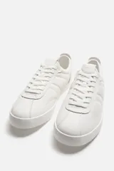 Zapatillas de cuero blanco con cordones y suela plana.