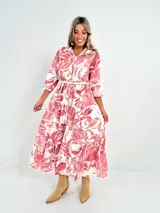 Vestido largo camisero con estampado floral en tonos rosados y blancos, con cuello camisero, manga 3/4 y falda escalonada. Incluye cinturón fino de soga.