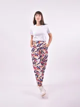 Pantalón babucha de tela estampada con hojas en tonos rosa, naranja y azul, con cintura elastizada y lazo para ajustar.