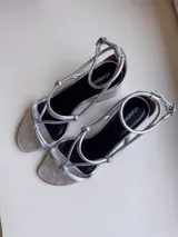 Sandalias negras de cuero con tiras finas con nudos en el empeine y pulsera con hebilla en el tobillo. Tacón bloque de 7cm.