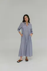 Vestido camisero largo a rayas verticales azules y blancas, con cuello camisero, mangas largas, abotonadura frontal completa, bolsillos laterales y corte holgado.