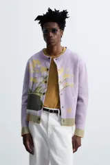 Cárdigan lila con diseño floral, cuello redondo, manga larga, rib en puños y ruedo, y cierre frontal con botones.