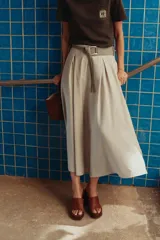 Falda midi color beige con textura rústica, tiro alto, pinzas delanteras, corte evasé y cinturón ancho con hebilla metálica.