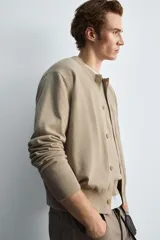 Cárdigan color beige de corte relaxed fit, tejido en hilatura con algodón y ramio. Tiene cuello redondo, manga larga, acabados en rib y cierre frontal de botonadura.