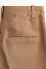 Pantalón de vestir color camel, de corte amplio, tiro alto y largo hasta el tobillo.